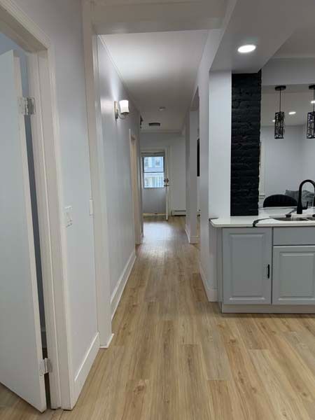 Bright hallway with white walls, light wood floors, and a small kitchen area on the right