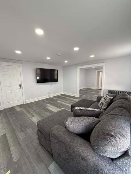 Modern gray living room with sectional sofa, wall-mounted TV, recessed lights, and open doorway