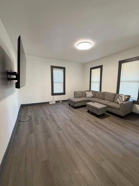 Modern living room with gray sectional sofa, wall-mounted TV, and large windows on wood flooring