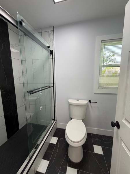 Small bathroom with glass shower, white toilet, and black-and-white tile floor