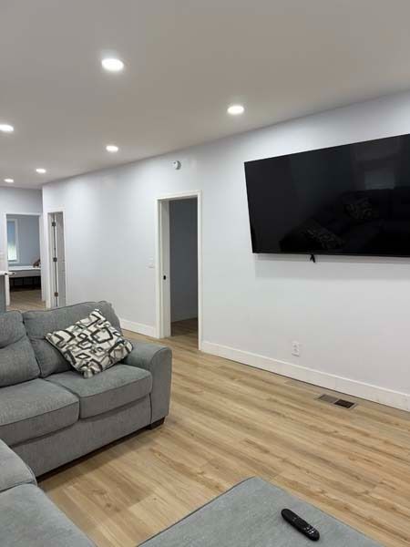 Modern living room with gray sofa, wall-mounted TV, recessed lights, and light wood flooring