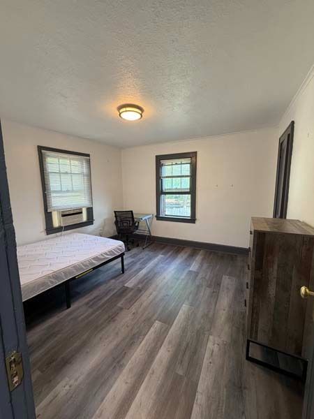 Small bedroom with bed, chair, dresser, and two windows in neutral tones