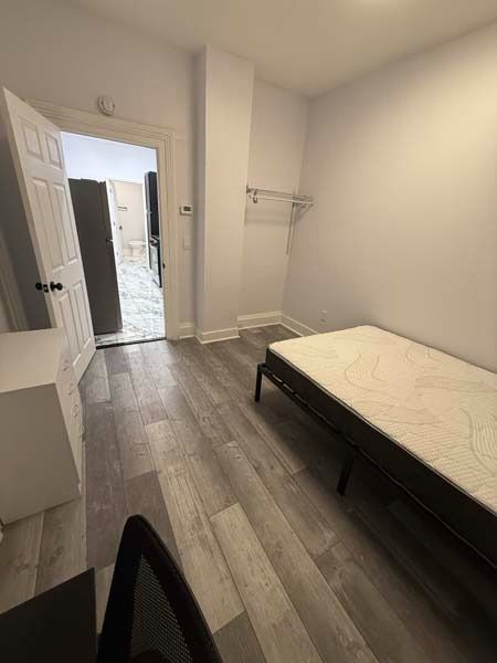 Small bedroom with a bed, gray wood floor, white walls, and an open door to a bathroom.