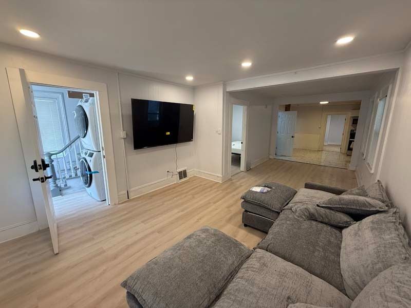 Modern living room with gray sectional, wall-mounted TV, and open doorway to a lit hallway
