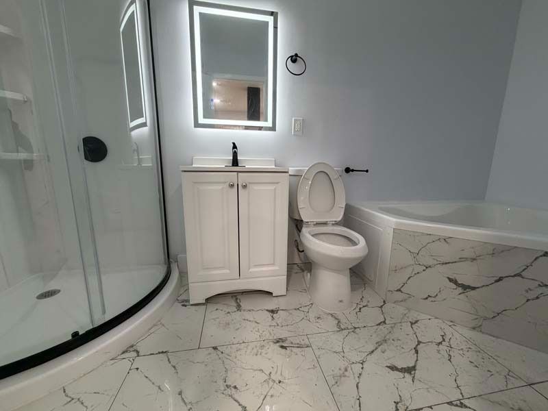Modern white bathroom with curved glass shower, vanity, toilet, tub, and marble-pattern floor and walls