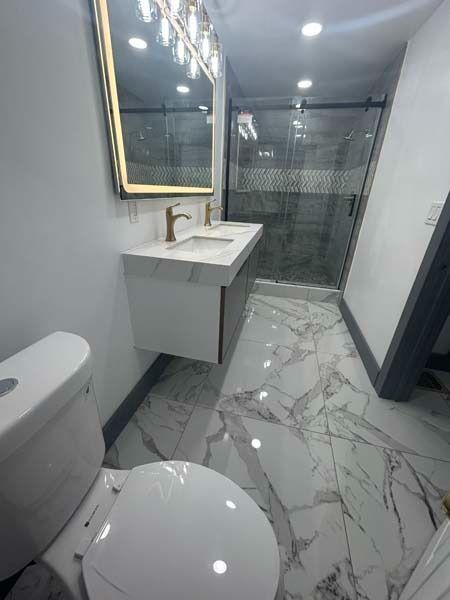 Small modern bathroom with marble tile, floating sink vanity, toilet, and glass shower door.