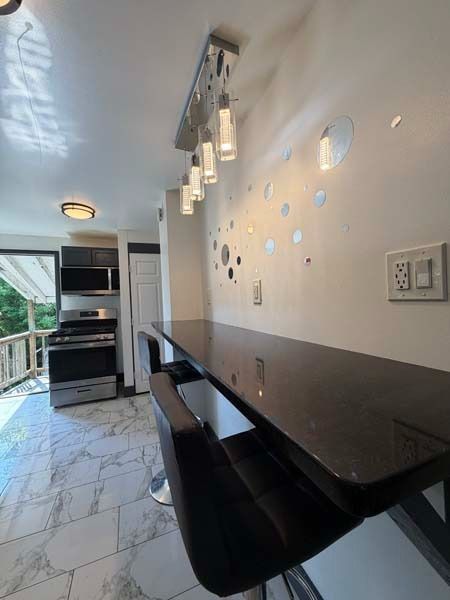 Modern hallway with black counter, pendant lights, marble floor, and wall decor leading to a kitchen area