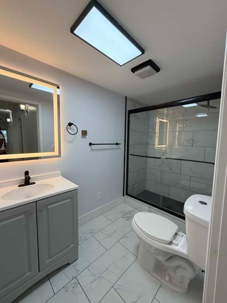 Modern bathroom with vanity, lit mirror, skylight, glass shower, and toilet