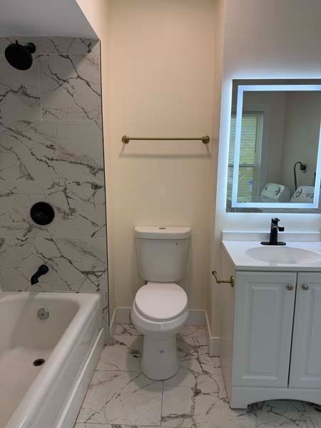 Bathroom with white marble tile, bathtub, toilet, towel bar, and vanity with sink and mirror.