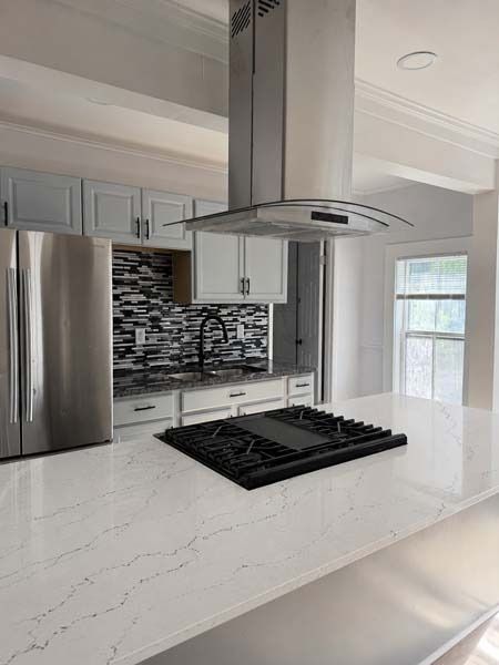Modern white kitchen with stainless steel appliances, marble island, and gas cooktop beneath a range hood