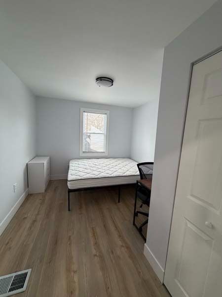 Small bedroom with a bed, desk, dresser, and window on light wood floors