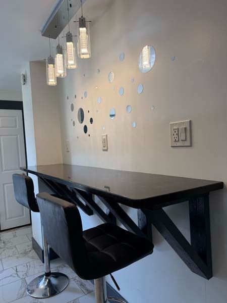 Modern breakfast bar with black stools and hanging pendant lights beside a wall with circular decor
