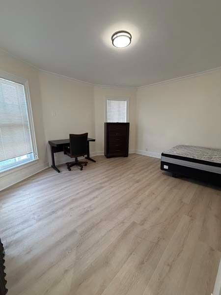 Empty bedroom with light wood floors, white walls, a desk and chair, dresser, and a bed along the right wall