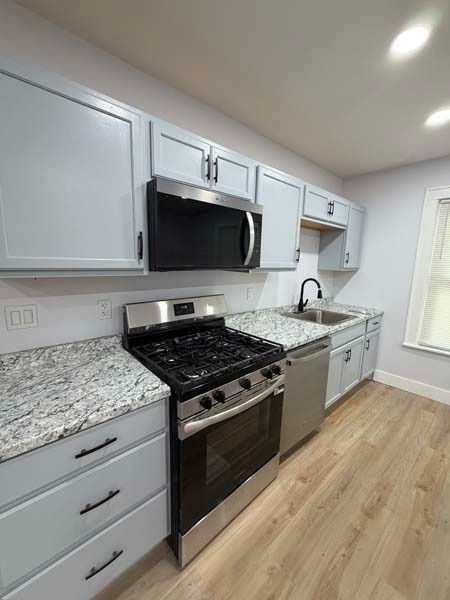 Bright modern kitchen with white cabinets, granite counters, stainless appliances, and wood flooring