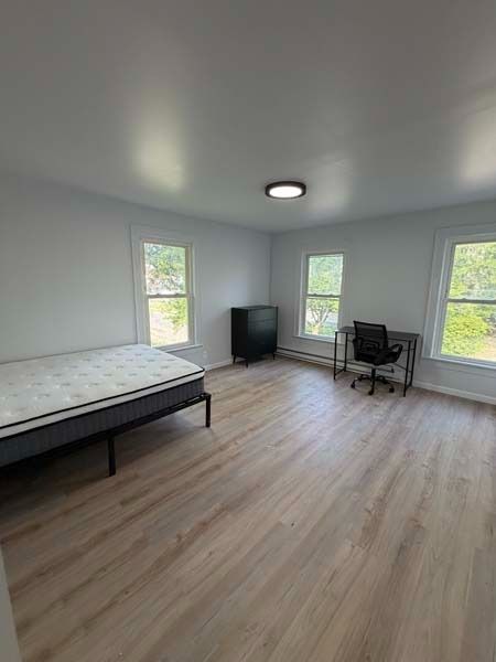 Spare bedroom with bed, desk, chair, dresser, and large windows on wood-look flooring.