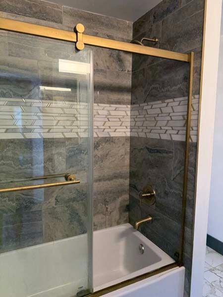 Glass shower enclosure with gold trim and tiled walls in a bathroom
