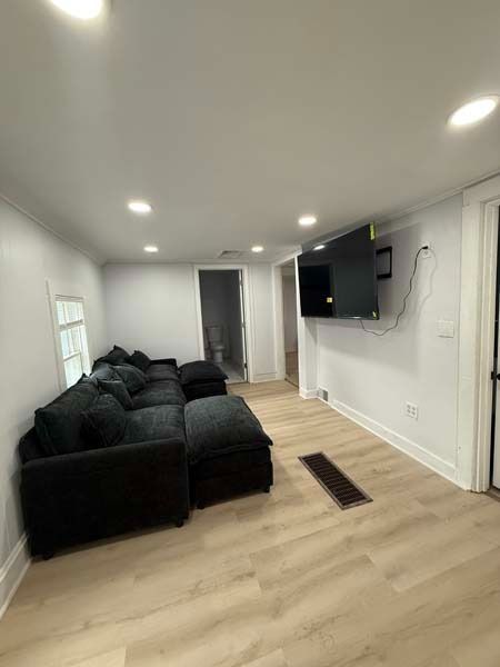 Bright living room with black sofas, wall-mounted TV, and light wood floors