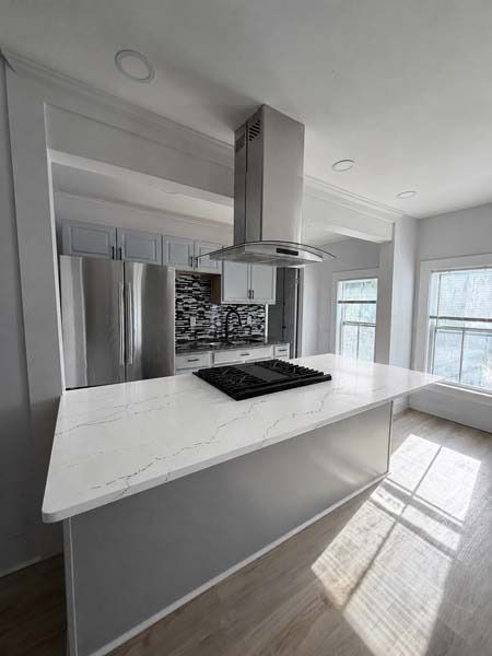 Modern white kitchen with marble island, stainless steel range hood, and bright window light