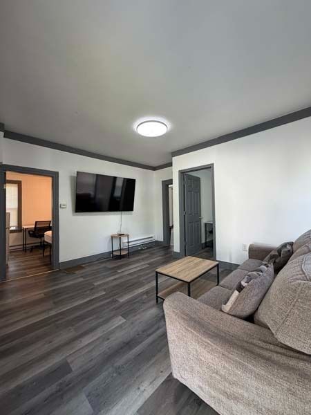 Modern living room with gray sofa, wall-mounted TV, dark floors, and white walls