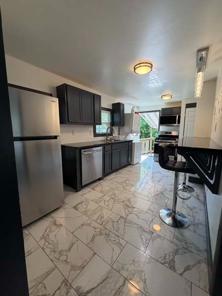 Modern kitchen with stainless steel appliances, dark cabinets, marble-look floor, and breakfast bar stools