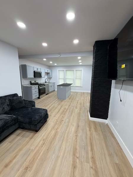 Modern open-concept living room with black sofa, kitchen, island, and wood flooring
