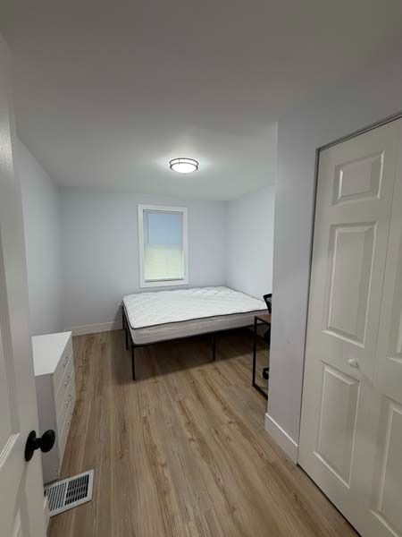 Small bedroom with a bed, white walls, wood floor, and a window with blinds.
