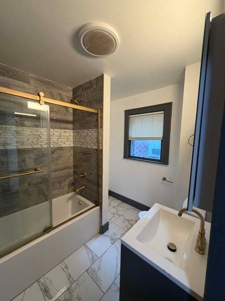 Small bathroom with glass shower, white vanity, window, and tiled floor.