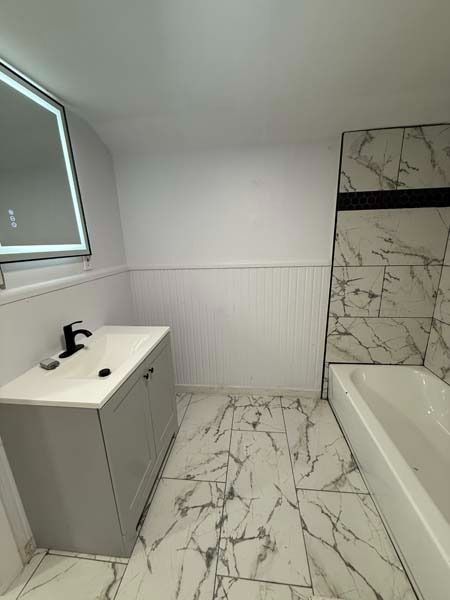 Modern bathroom with marble tile, vanity sink, window, and bathtub