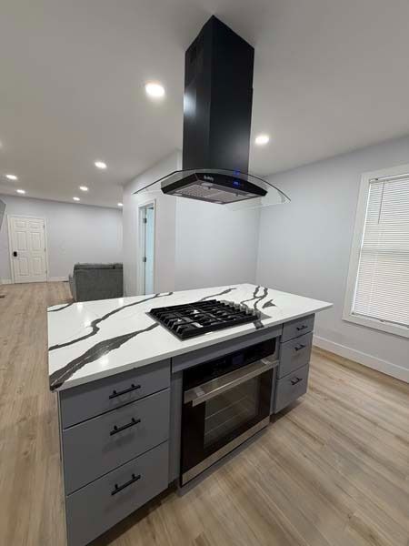 Modern kitchen island with marble countertop, black range hood, and gray cabinets in a bright room