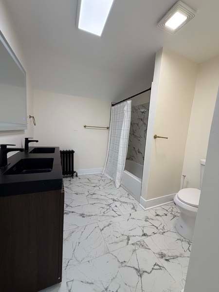 Modern bathroom with marble tile floor, black vanity, glass shower door, and toilet under skylight lighting