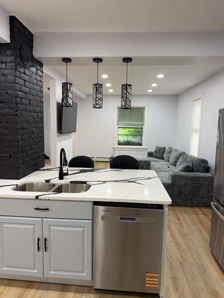 Open-plan kitchen and living room with white island, black brick wall, gray sofa, and pendant lights