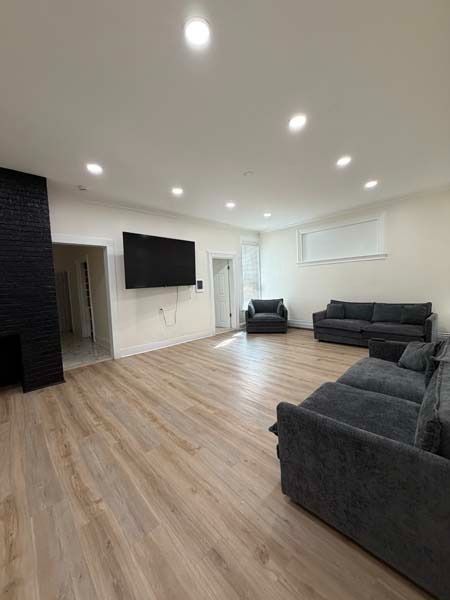 Spacious living room with gray sofas, wall-mounted TV, recessed lights, and wood-look flooring.
