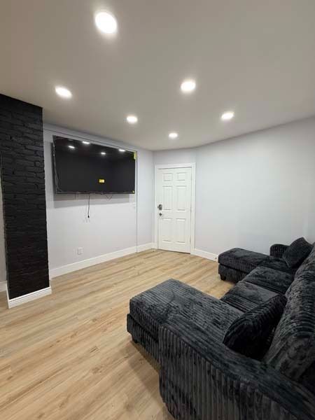 Modern living room with wall-mounted TV, recessed lights, white door, and black sofa on wood flooring