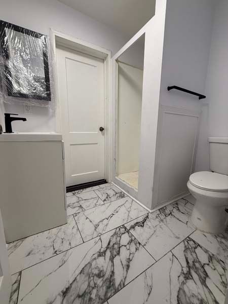 Modern bathroom with marble tile, white vanity, shower stall, and toilet