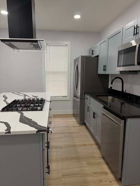 Modern gray kitchen with stainless steel appliances, black countertops, and a gas cooktop