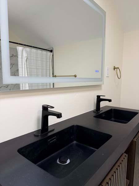 Modern bathroom vanity with double black sinks, matte black faucets, and a wall mirror