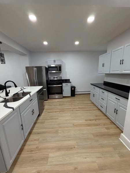 Bright modern kitchen with white cabinets, gray counters, and light wood floors