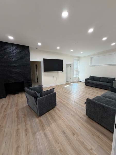Modern living room with black sofa, armchairs, wall-mounted TV, fireplace, and light wood floors