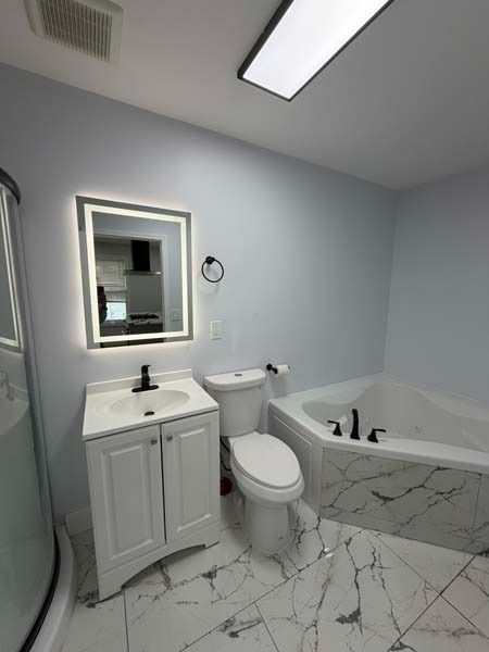 Modern bathroom with white marble tile, vanity, toilet, and bathtub under bright lighting