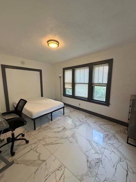 Small bedroom with a bed, office chair, window, and marble-pattern tile floor.