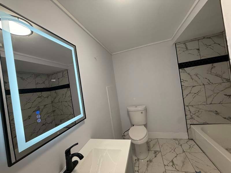 Modern bathroom with large mirror, toilet, bathtub, and white marble-pattern tile walls and floor