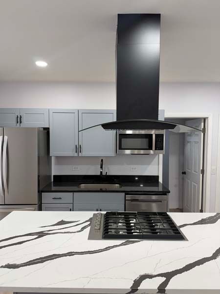 Modern kitchen with white cabinetry, stainless steel appliances, and a black range hood over a marble island.
