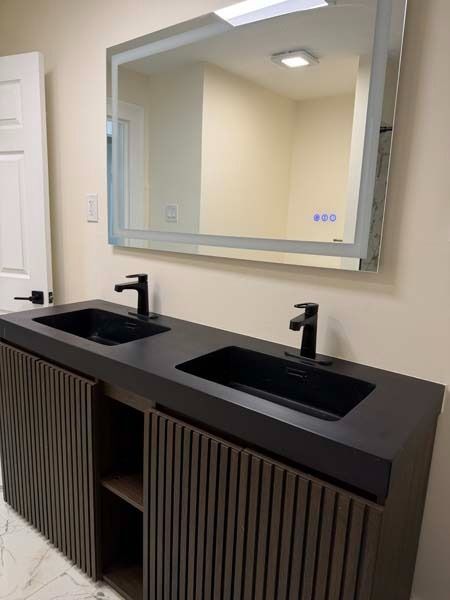 Modern restroom vanity with two black sinks, dark ribbed cabinets, and a large mirror above.