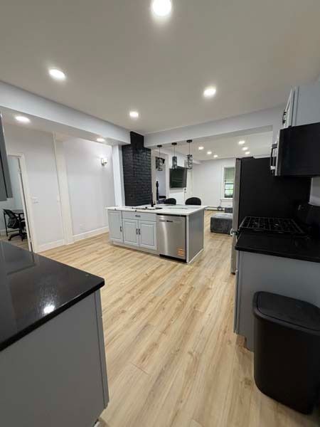 Modern kitchen with light wood floors, white cabinets, black countertops, and stainless steel appliances