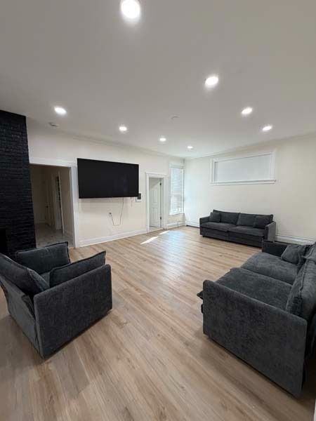 Modern living room with dark sofas, wall-mounted TV, wood floors, and recessed ceiling lights