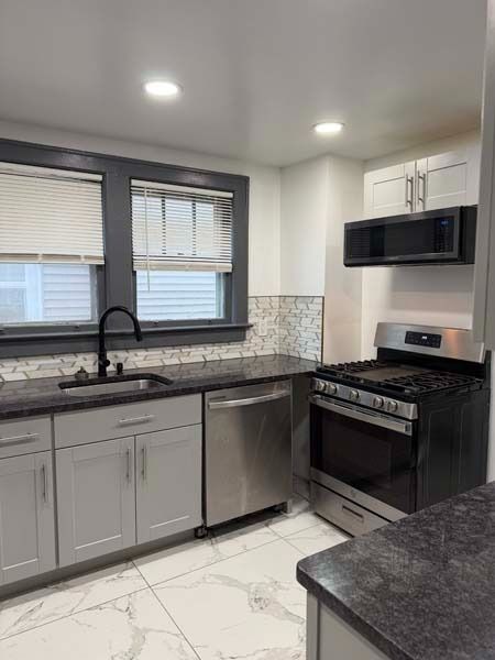 Modern kitchen with white cabinets, gray countertops, stainless appliances, and large windows