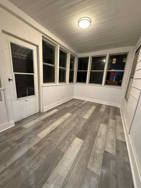 Empty enclosed porch with gray plank flooring, white walls, windows, and a single ceiling light.