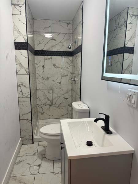 Small modern bathroom with marble-pattern tile, toilet, sink, and mirror.