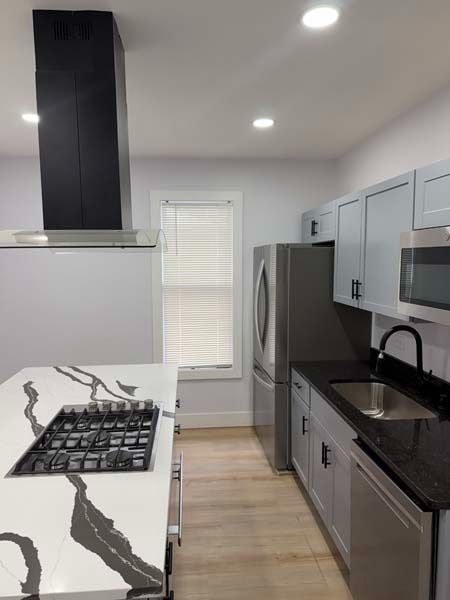 Modern kitchen with gray cabinets, black countertops, stainless steel appliances, and a marble-pattern island.
