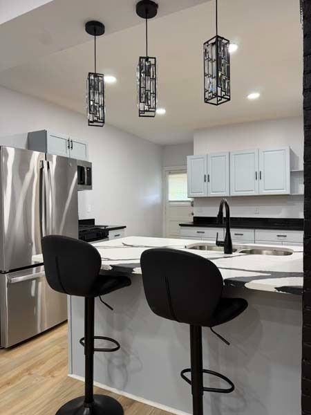 Modern kitchen with white cabinets, stainless fridge, island, black stools, and three pendant lights